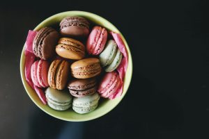 : Colorful French macarons dessert arranged in a green bowl with pink tissue paper on a dark background.