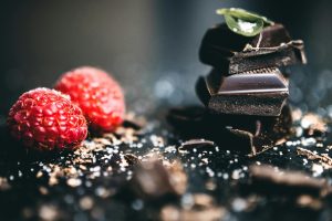 Close-up of rich dark chocolate pieces stacked with fresh raspberries, perfect ingredients for a gourmet dessert.