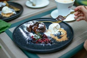 Indulgent chocolate lava cake dessert served with vanilla ice cream, berries, and powdered sugar on a black plate.